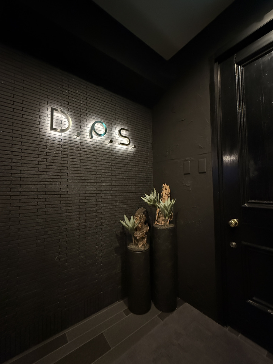 暗いタイルの壁に光るD.P.S.のマーク。鉢植えが二つ、その横に黒い扉。